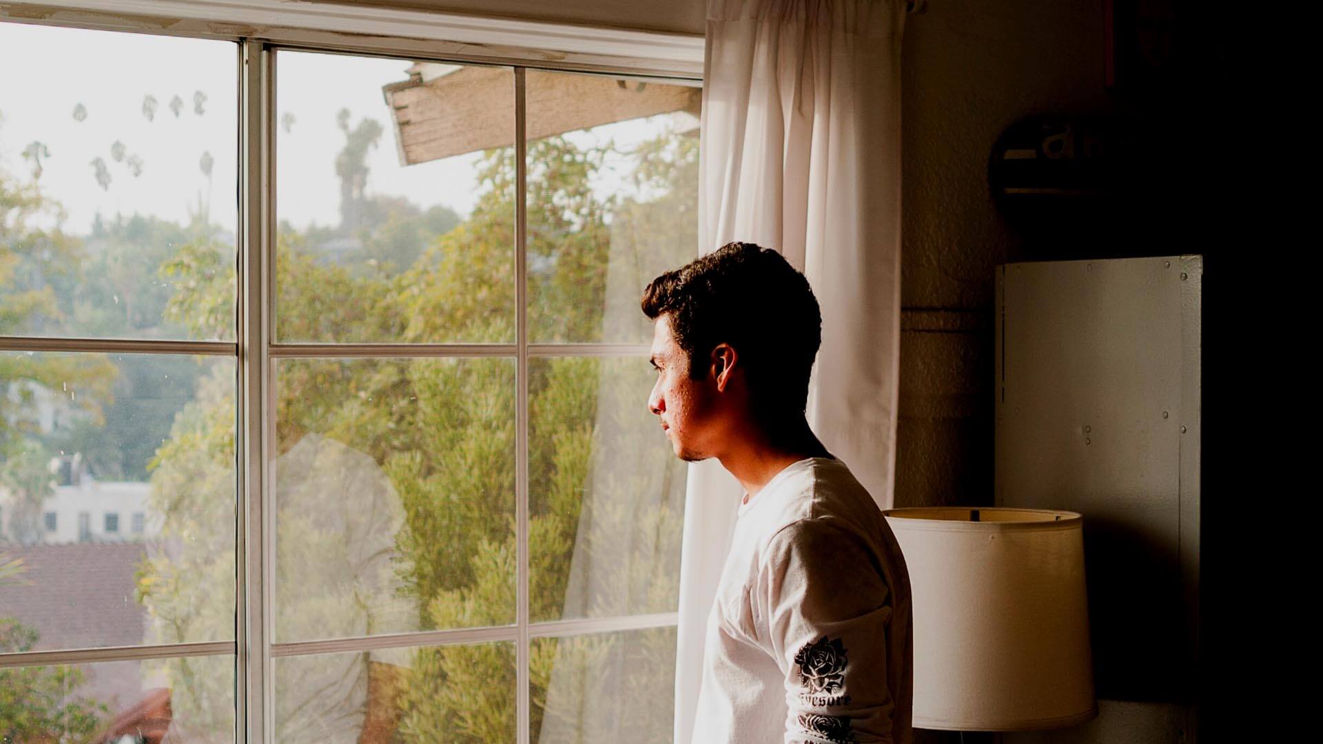 man wearing gray and black crew-neck shirt standing and looking out window
